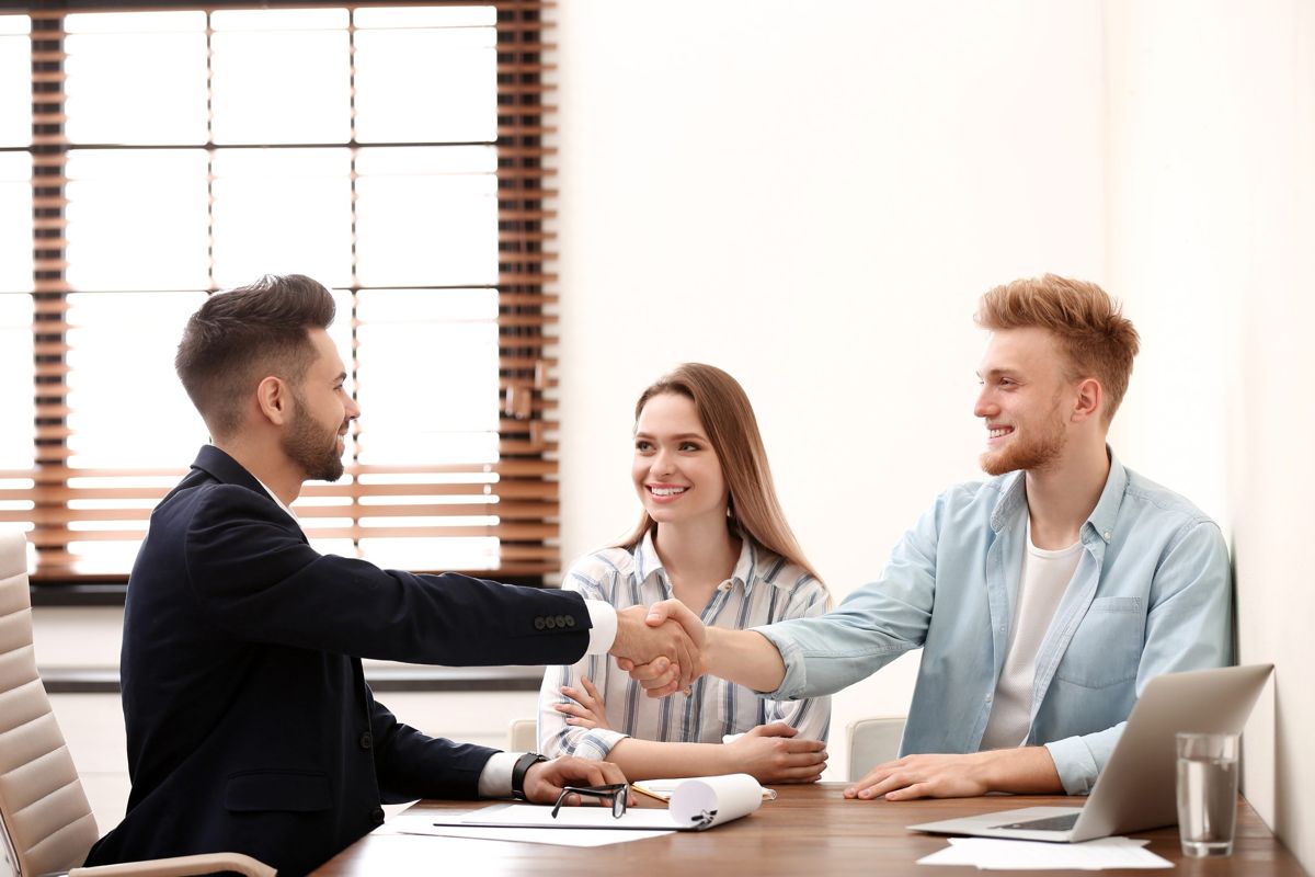 Three people shaking hands across a desk